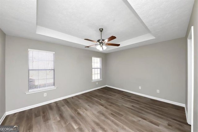 unfurnished room with a raised ceiling, ceiling fan, dark wood-type flooring, and a textured ceiling