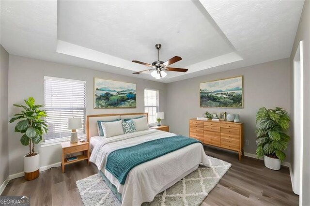 bedroom featuring hardwood / wood-style floors, a raised ceiling, and ceiling fan