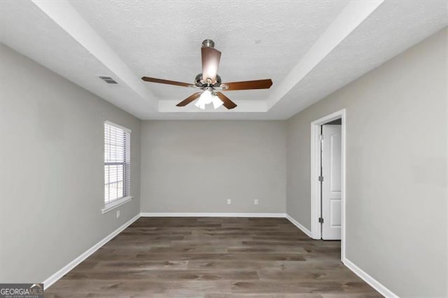 unfurnished room featuring a tray ceiling, ceiling fan, dark wood-type flooring, and a textured ceiling