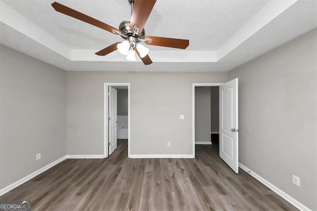 unfurnished bedroom with a textured ceiling, a tray ceiling, ceiling fan, and dark wood-type flooring