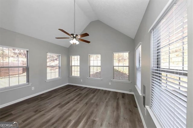 spare room with a healthy amount of sunlight, ceiling fan, dark wood-type flooring, and vaulted ceiling