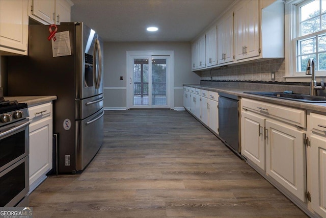 kitchen featuring sink, white cabinetry, hardwood / wood-style flooring, stainless steel appliances, and backsplash