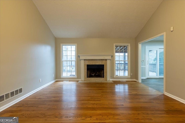 unfurnished living room with a tile fireplace, lofted ceiling, dark hardwood / wood-style floors, and a textured ceiling