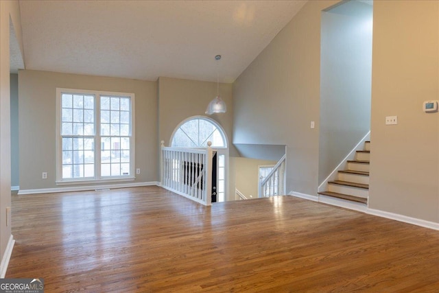 unfurnished living room with wood-type flooring and high vaulted ceiling