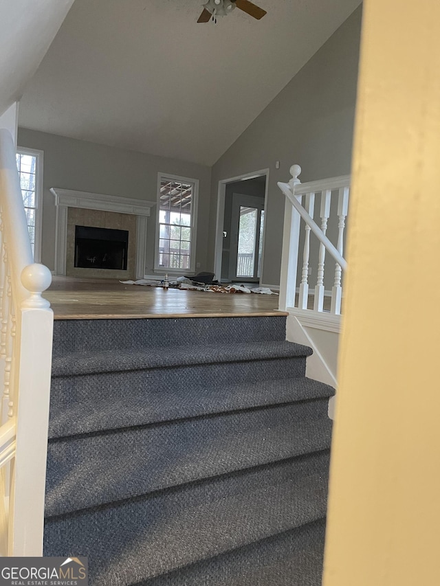 staircase with ceiling fan, lofted ceiling, plenty of natural light, and a tiled fireplace