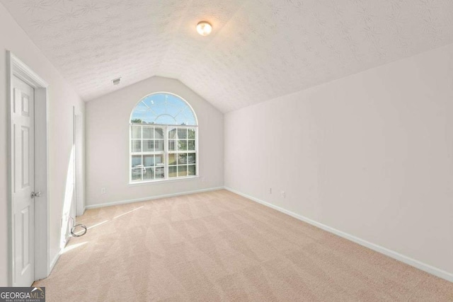 spare room featuring a textured ceiling, light colored carpet, and vaulted ceiling