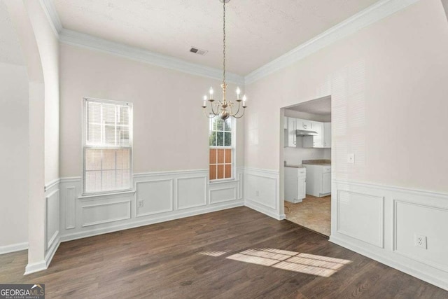 unfurnished dining area featuring dark hardwood / wood-style flooring, ornamental molding, a textured ceiling, and an inviting chandelier