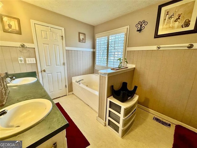 bathroom with a bathing tub, wood walls, vanity, and a textured ceiling