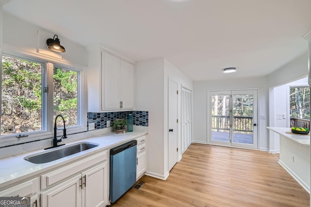 kitchen featuring sink, white cabinetry, decorative backsplash, stainless steel dishwasher, and light wood-type flooring