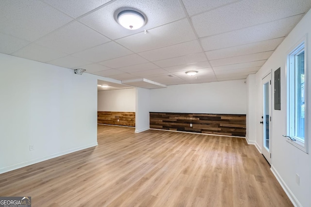 unfurnished room with a paneled ceiling, wooden walls, and light hardwood / wood-style flooring