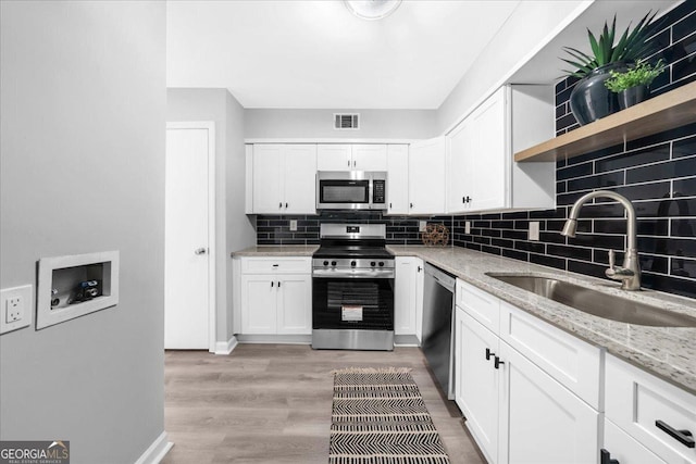 kitchen with backsplash, sink, appliances with stainless steel finishes, light stone counters, and white cabinetry