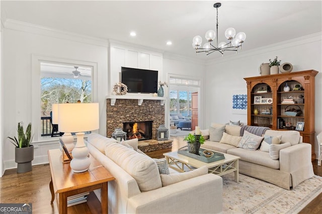 living room featuring a fireplace, wood-type flooring, ceiling fan with notable chandelier, and ornamental molding