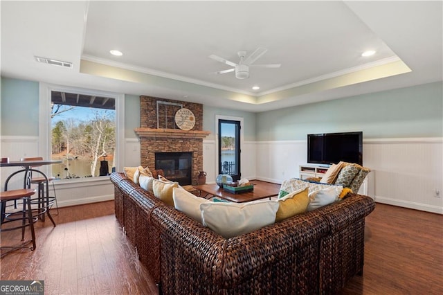 living room featuring a tray ceiling, a stone fireplace, dark hardwood / wood-style flooring, and ornamental molding