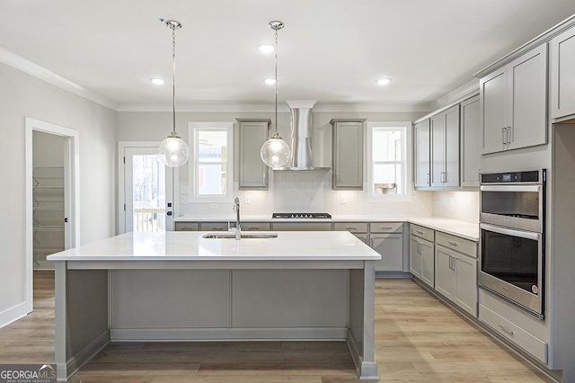 kitchen featuring wall chimney exhaust hood, double oven, sink, gray cabinets, and hanging light fixtures