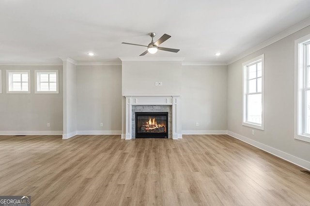 unfurnished living room with a stone fireplace, plenty of natural light, crown molding, and ceiling fan