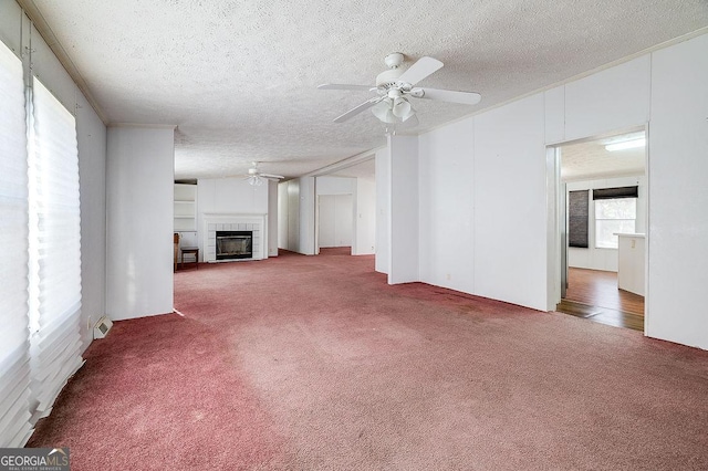 unfurnished living room featuring ceiling fan, a tiled fireplace, a textured ceiling, and carpet flooring