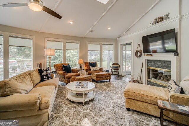 living room featuring vaulted ceiling, hardwood / wood-style flooring, a stone fireplace, and ceiling fan