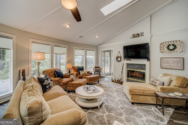 living room with vaulted ceiling with skylight, plenty of natural light, ceiling fan, and a stone fireplace