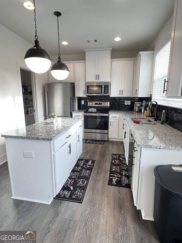 kitchen with a kitchen island, appliances with stainless steel finishes, pendant lighting, and white cabinets