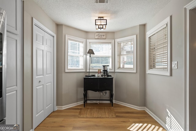 interior space featuring light wood-style floors, visible vents, baseboards, and a textured ceiling