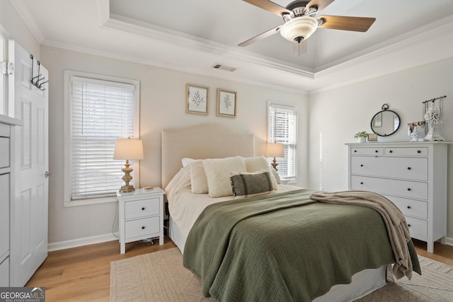 bedroom with crown molding, a raised ceiling, visible vents, light wood-style flooring, and baseboards