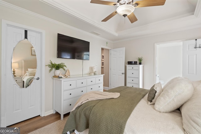 bedroom featuring wood finished floors, visible vents, a ceiling fan, ornamental molding, and a tray ceiling