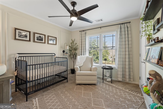 carpeted bedroom featuring a crib, visible vents, baseboards, ceiling fan, and ornamental molding