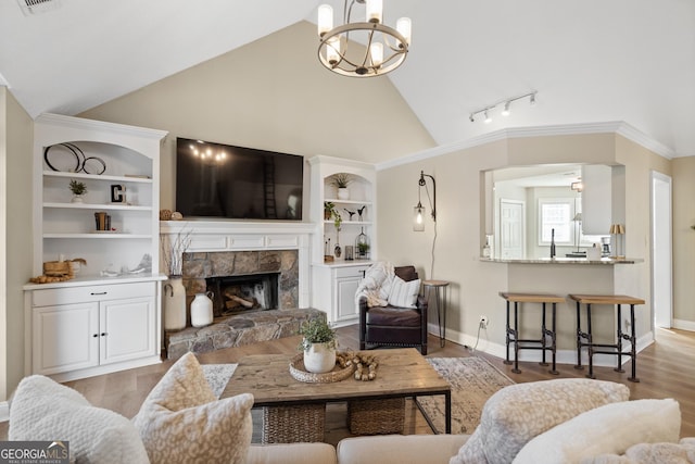 living room featuring vaulted ceiling, light hardwood / wood-style flooring, built in shelves, an inviting chandelier, and a fireplace