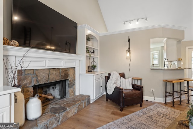 sitting room featuring built in shelves, a fireplace, baseboards, vaulted ceiling, and light wood finished floors