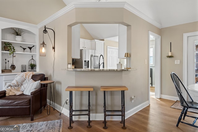 kitchen with a peninsula, white cabinetry, stainless steel refrigerator with ice dispenser, light stone countertops, and a kitchen bar