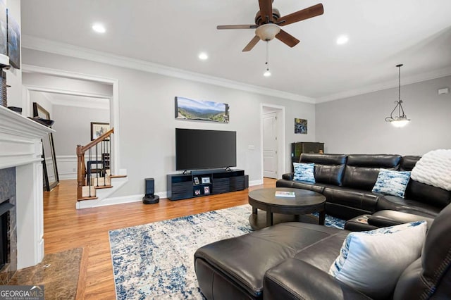 living room with crown molding, wood-type flooring, a premium fireplace, and ceiling fan