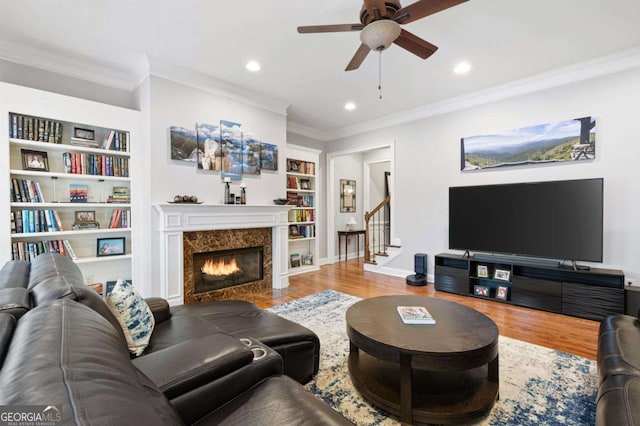 living room featuring built in shelves, wood-type flooring, ornamental molding, and a high end fireplace