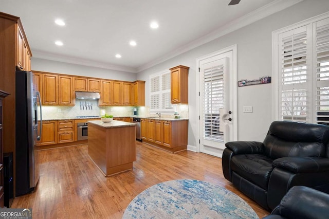 kitchen with appliances with stainless steel finishes, decorative backsplash, ornamental molding, a center island, and light wood-type flooring