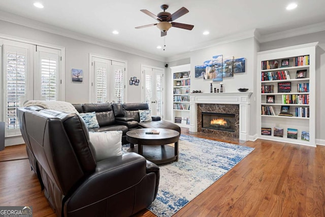 living room with built in shelves, ornamental molding, ceiling fan, a premium fireplace, and hardwood / wood-style floors