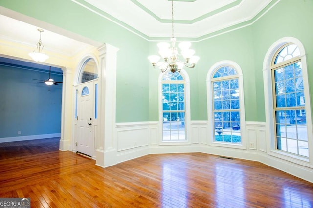 unfurnished dining area with wood-type flooring, ceiling fan with notable chandelier, and ornamental molding