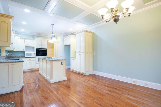 kitchen with a center island, coffered ceiling, an inviting chandelier, pendant lighting, and white appliances