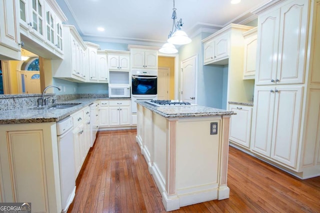 kitchen with a center island, sink, light stone counters, pendant lighting, and white appliances