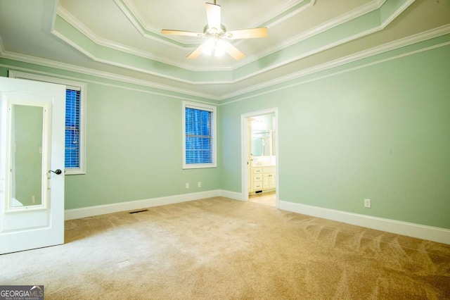 carpeted spare room with a tray ceiling, ceiling fan, and ornamental molding