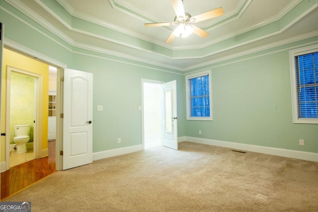 empty room with a tray ceiling, light colored carpet, and ornamental molding