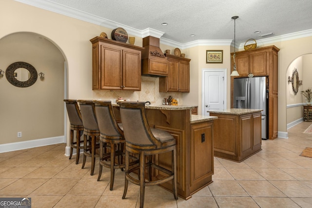 kitchen featuring stainless steel fridge with ice dispenser, a kitchen island, light tile patterned floors, and ornamental molding