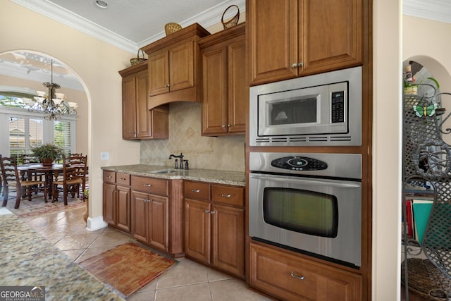 kitchen featuring appliances with stainless steel finishes, backsplash, light stone counters, a chandelier, and light tile patterned flooring