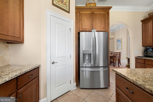 kitchen featuring stainless steel fridge with ice dispenser, light tile patterned floors, light stone counters, and ornamental molding