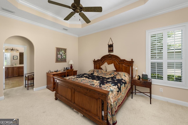 carpeted bedroom with ceiling fan, a raised ceiling, ornamental molding, and ensuite bathroom