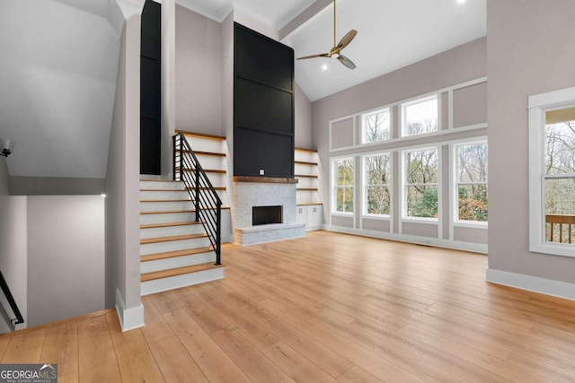 unfurnished living room with ceiling fan, light hardwood / wood-style flooring, high vaulted ceiling, beamed ceiling, and a fireplace