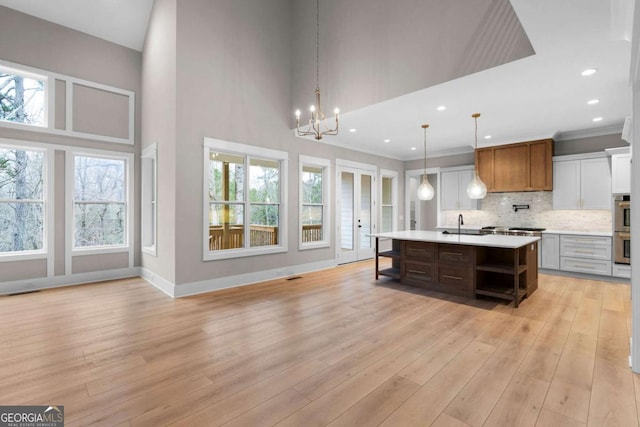 kitchen featuring pendant lighting, a high ceiling, a center island with sink, tasteful backsplash, and a chandelier