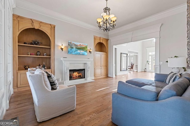 living room with built in shelves, hardwood / wood-style flooring, ornamental molding, and an inviting chandelier