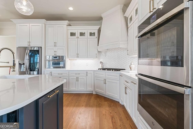 kitchen featuring hanging light fixtures, white cabinetry, custom range hood, and appliances with stainless steel finishes