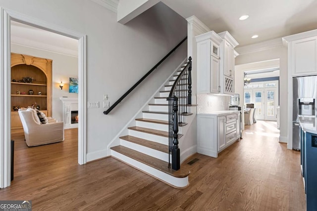 stairway with built in shelves, hardwood / wood-style floors, and ornamental molding