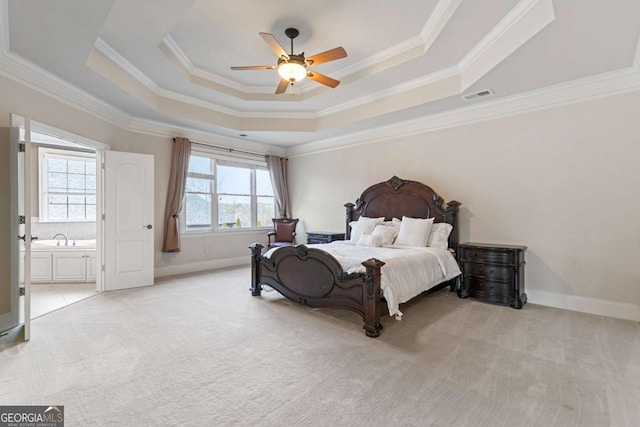 bedroom featuring ceiling fan, ensuite bathroom, light colored carpet, a tray ceiling, and ornamental molding