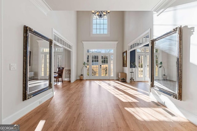 entrance foyer with french doors, crown molding, hardwood / wood-style floors, a towering ceiling, and a chandelier